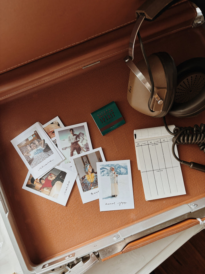 Vintage suitcase with Catholic Saint Polaroid photos, headphones, and a notepad.